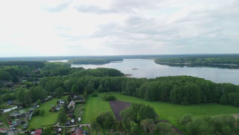 Beautiful-aerial-view-of-a-tranquil-lake-surrounded-by-lush-green-trees-and-a-small-village-with-houses-and-gardens