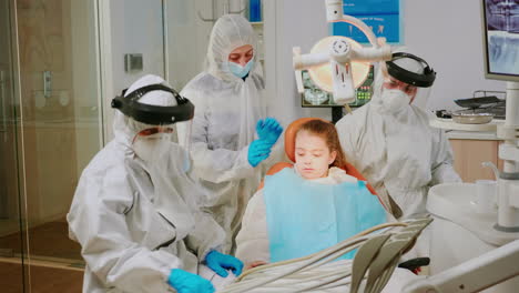 little patient in ppe suit lying on chair with open mouth during dental examination