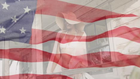 Animation-of-waving-flag-of-america-over-african-american-woman-relaxing-outside-beach-house