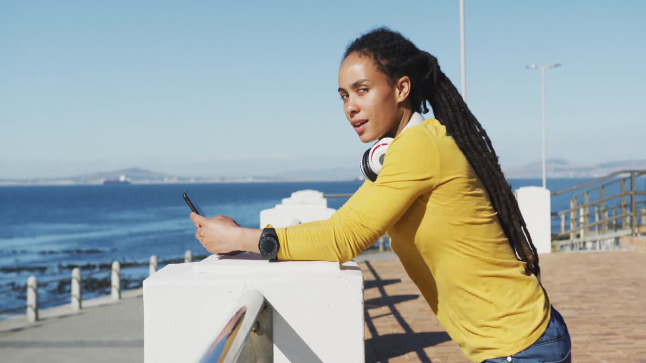 African american woman using smartphone on promenade by the sea