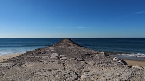 Pov walk on emtpy beach along endless old stone jetty in front of the sea