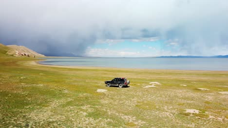 A-stunning-drone-captures-the-beauty-of-Chatyr-Kol-Kyrgyzstan-in-the-summer,-showcasing-storm-clouds-over-the-lake-and-car