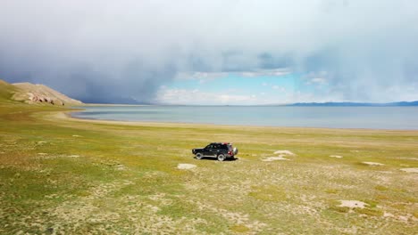 a stunning drone captures the beauty of chatyr kol kyrgyzstan in the summer, showcasing storm clouds over the lake and car