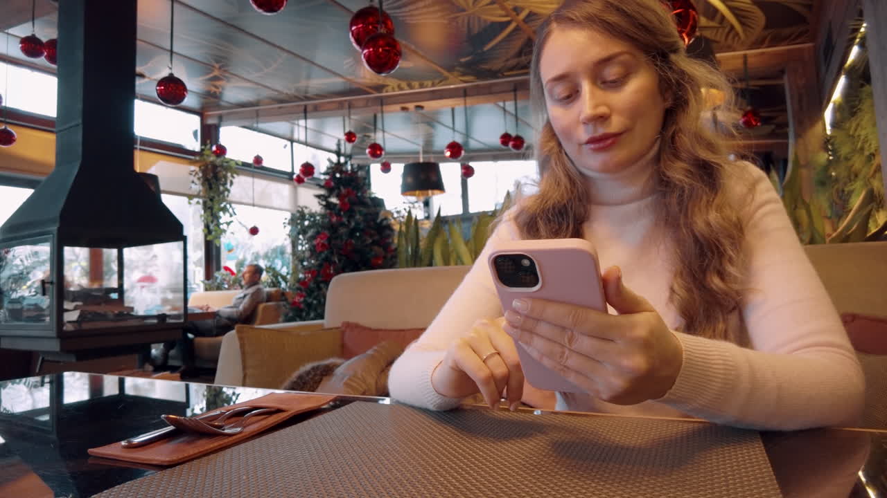 Blonde woman scrolling on her phone at a cafe decorated for Christmas