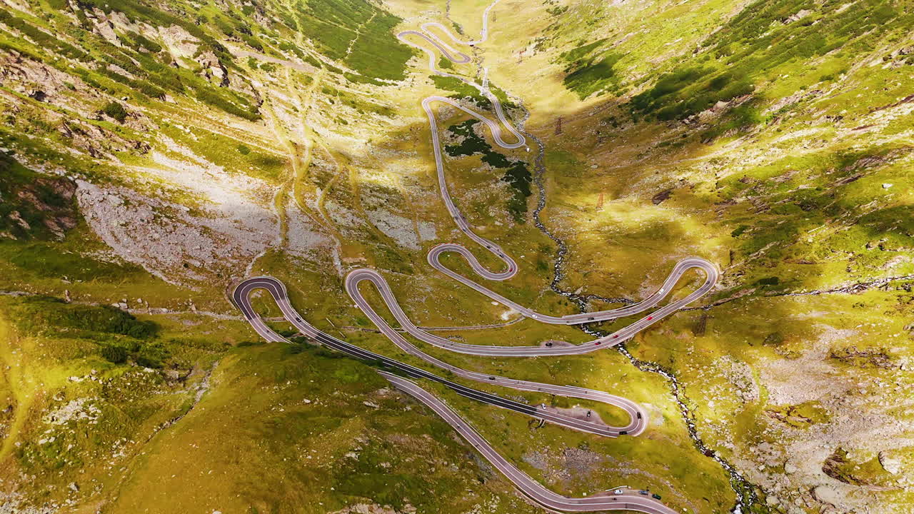 Spectacular Transfagarash highway in the valley among the rocks. Cars ride by the wavy road. Aerial view