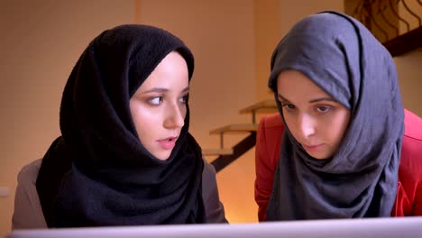 closeup portrait of two young female muslim office workers in hijabs discussing the data in front of the laptop. teamwork of arabian businesswomen