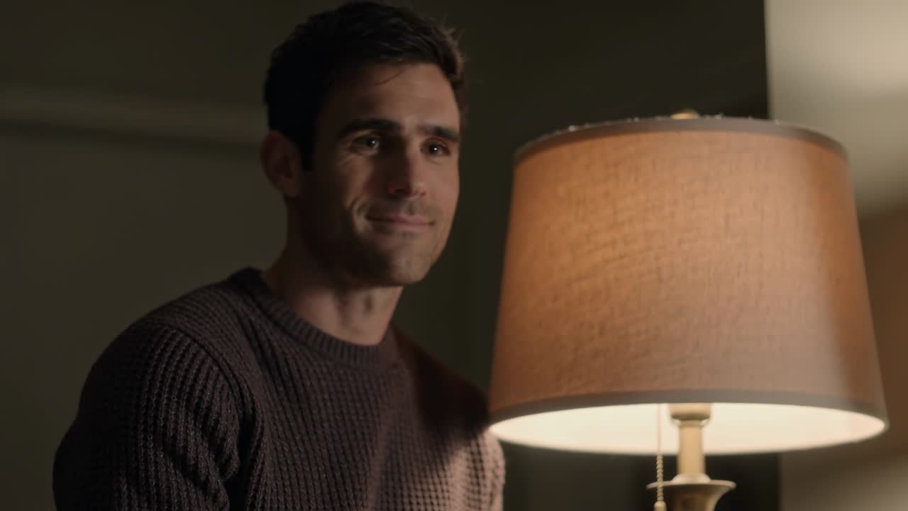 Pulling focus, man wearing dark brown knit sweater smiling softly at home with lamp pull chain