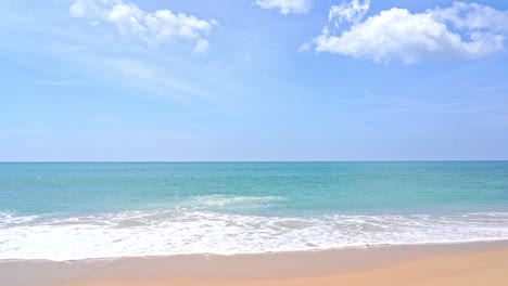 empty sandy beach and emerald tranquil sea foamy tides rolling on sand on uninhabited island in thailand, cloudy sky, vacation template, copy space minimalistic no people