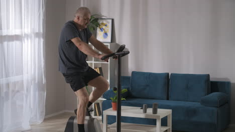 keeping fit and good physical condition by workout on stationary bike middle aged man is training alone at home healthy lifestyle at self-isolation