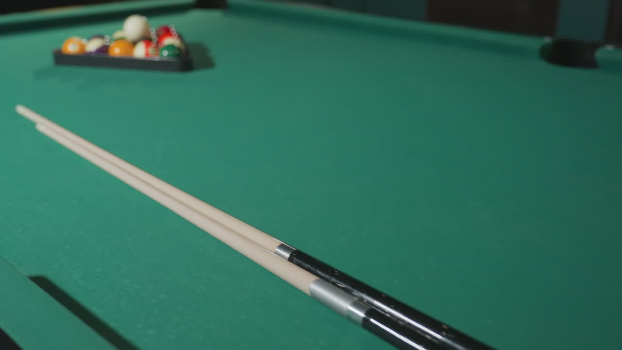 Colorful billiard balls neatly arranged in triangle rack on green pool table with two cue sticks laid across the table, capturing a moment of preparation for a game in a cozy setting