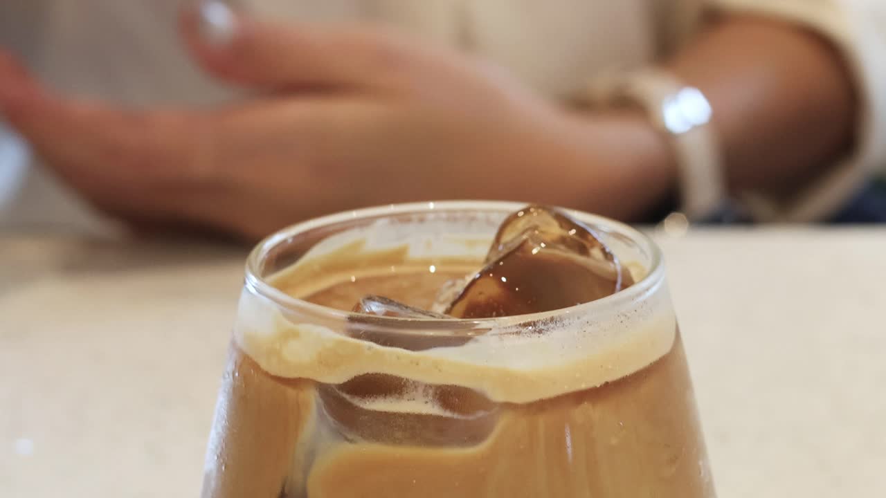 Hand stirring iced coffee with a straw