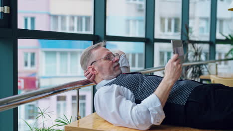 joyful senior manager relaxing on table leaning near window with tablet. modern office, leaning back watching tablet. video with businesspeople.