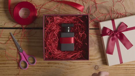 fotografía cenital del hombre envolviendo regalos de san valentín romántico presente de perfume en caja en la mesa