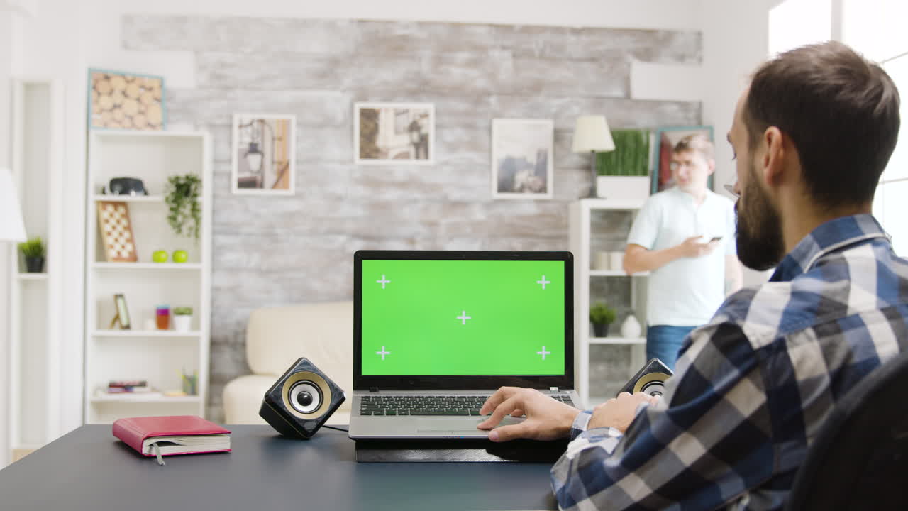 Man working on laptop with green screen at home office