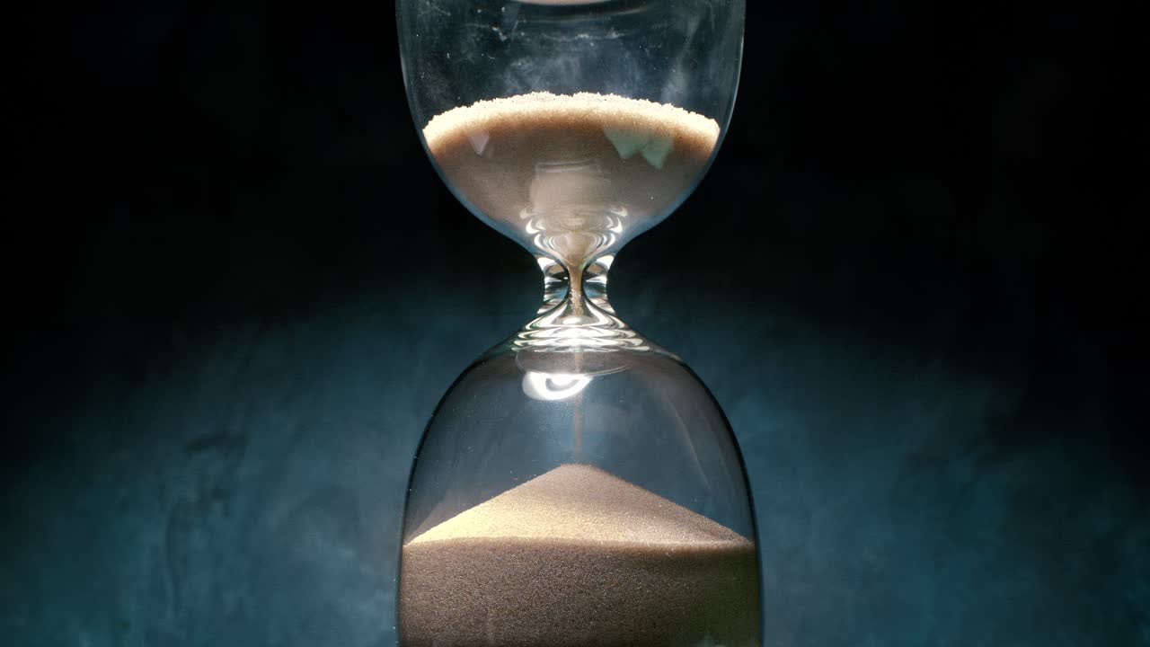 Hourglass with grains of sand on a dark background. Shot on super slow motion camera 1000 fps.