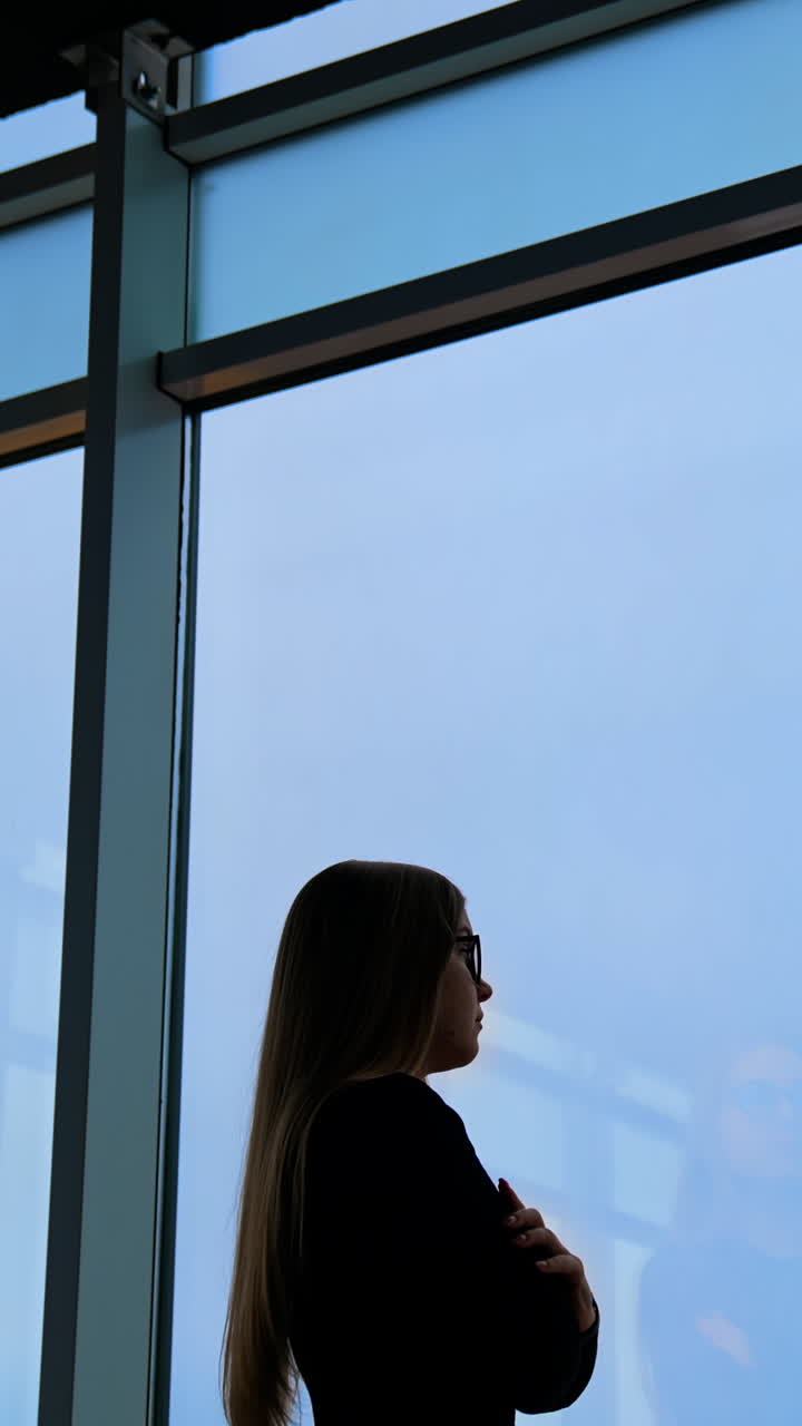 Pensive businesswoman dressed in formal apparel standing near panoramic window in enterprise company Vertical video