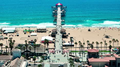 drone view flying over the pier in huntington beach california with some people walking around and cars driving down pch, pacific coast highway