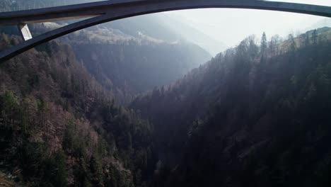 aerial flying underneath tamina bridge in between forested valley bathed in morning sunlight in st gallen region of switzerland