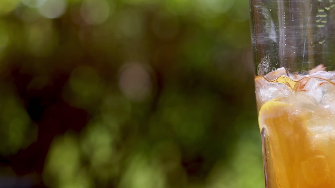 A refreshing orange beverage with ice cubes and a straw against a blurred green background.