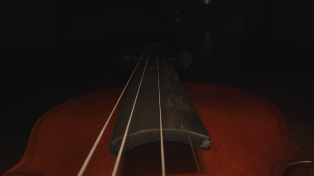 Slider shot down the neck of a violin, as the headstock disappears into mysterious darkness.