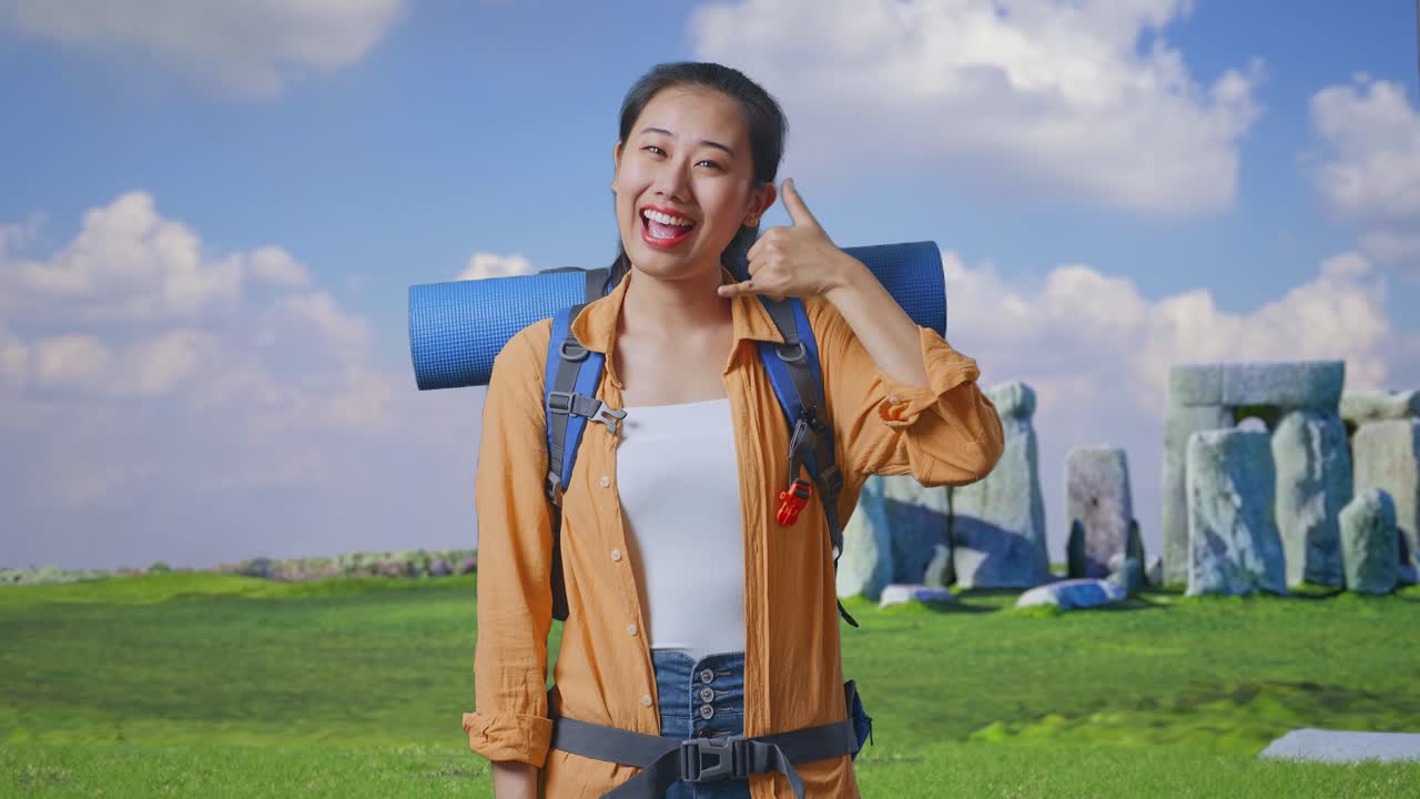 Asian Female Hiker With Mountaineering Backpack Smiling And Showing Call Me Gesture While Traveling In Stonehenge