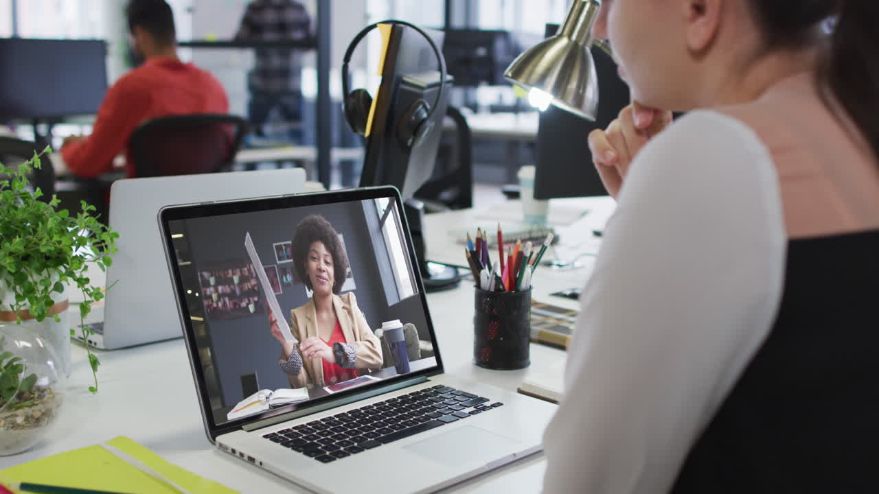Caucasian woman having a video call on laptop with female colleague at office