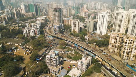 Highway-winds-across-Mumbai-India-passing-over-construction-site,-aerial-cityscape