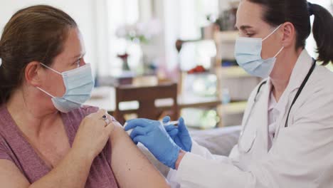 caucasian woman and female doctor wearing face masks, vaccinating