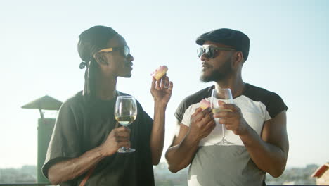 gay couple standing on rooftop with glasses of wine and donuts