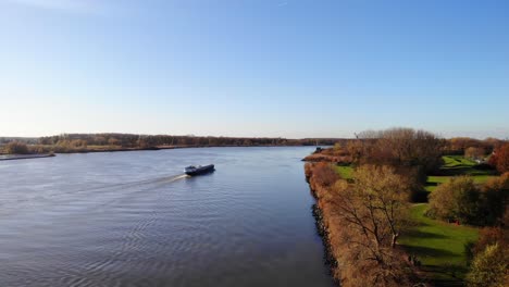 aerial rising from autumnal path next to oude maas with ship going past in background