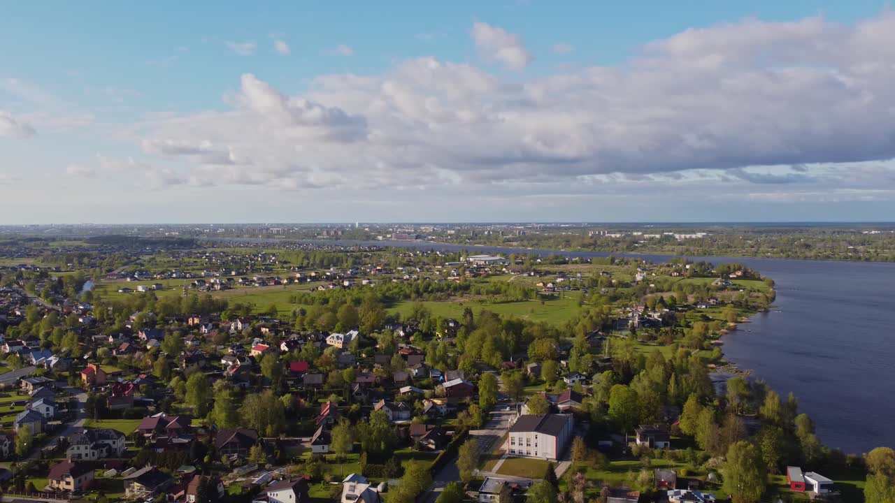 Residential streets stretch across quiet spring suburb with parked cars and green areas, aerial pan to river