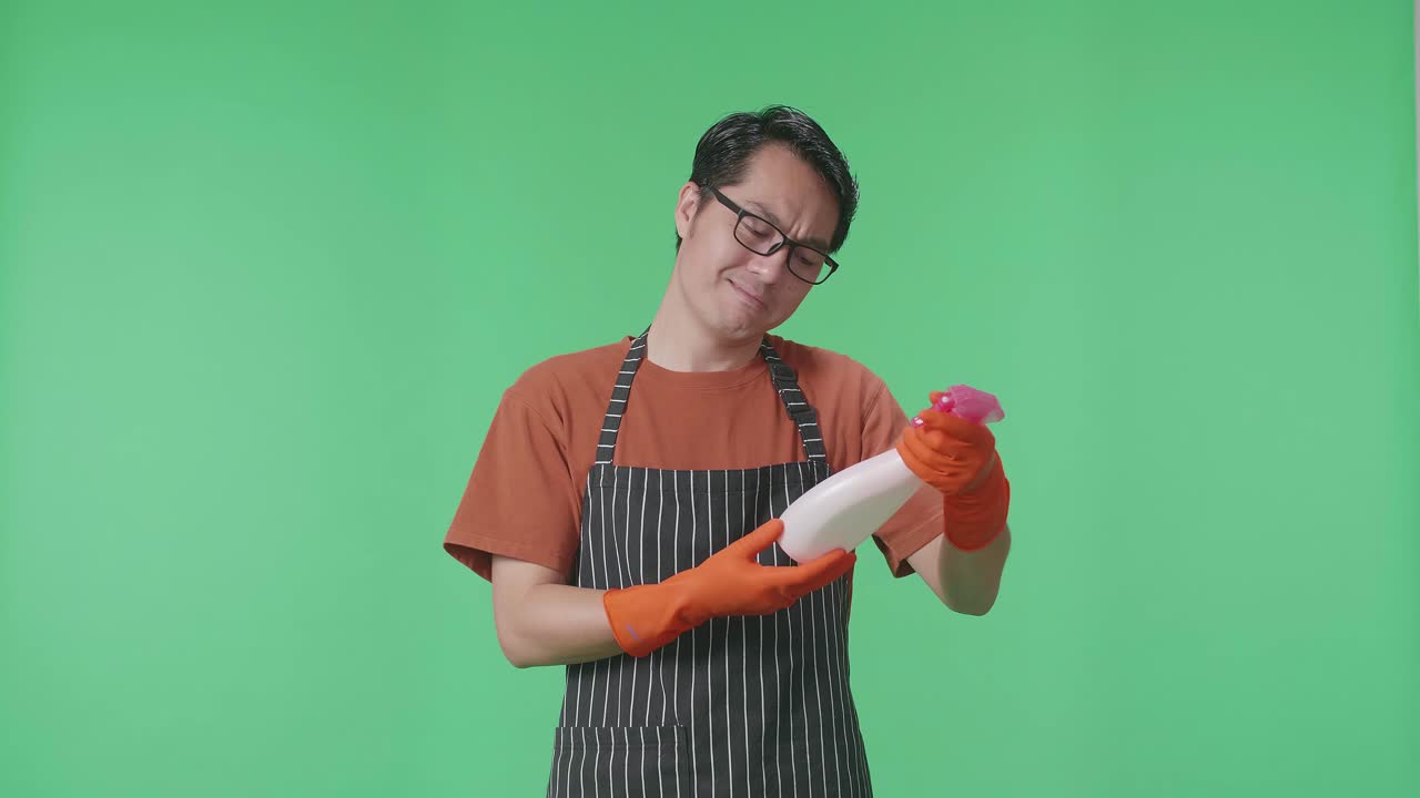 손에 스프레이를 들고 있는 아시안 남성 집주인이 그린 스크린 스튜디오에서 카메라를 향해 엄지손가락을 내려다보고 있다.