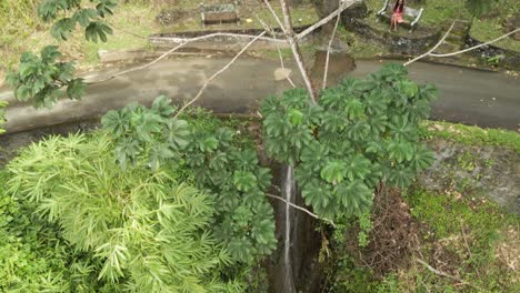 Aerial-view-of-a-young-lady-sitting-on-a-bench-next-to-a-waterfall-flowing-from-the-mountain