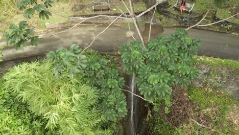 vista aérea de una joven sentada en un banco junto a una cascada que fluye desde la montaña