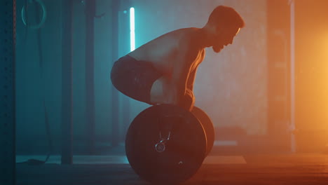 athletic shirtless man training doing power strength and endurance exercises with barbell. workout in the hardcore gym in slow motion