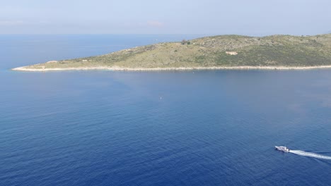 vista de avión no tripulado en albania volando sobre el océano azul claro con una pequeña isla verde y un pequeño barco que pasa en un día soleado