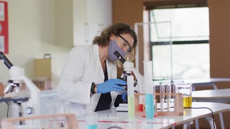 Female-teacher-wearing-face-mask-using-microscope-at-laboratory-at-school