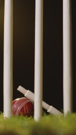 Vertikales-Video-Cricket-Stillleben-Mit-Nahaufnahme-Von-Bügeln,-Die-Auf-Einem-Ball-Im-Gras-Hinter-Stümpfen-Ruhen-1