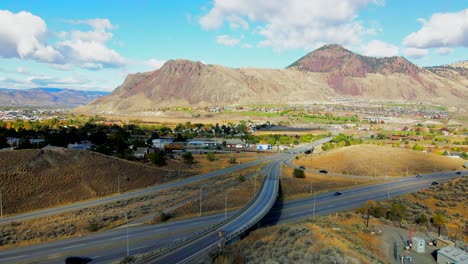 Dolly-In-Drohnenaufnahme-Von-Brücken-Und-Dem-Highway-1-Und-Dem-Yellowhead-Highway-5-In-Kamloops,-BC,-Kanada,-An-Einem-Bewölkten-Tag-In-Einer-Wüstenstadt-Mit-Fahrenden-Autos-Und-Sattelschleppern-Und-Mount-Paul-Im-Hintergrund