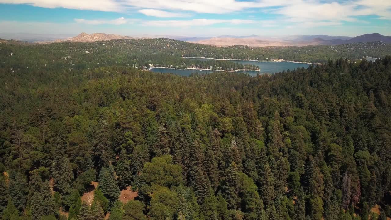 Aerial flyover forest ridge to reveal pristine lake nestled in the mountains. 4K