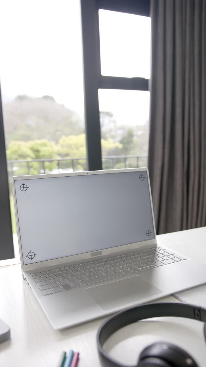 Vertical video of laptop with copy space on screen and headphones on desk, slow motion
