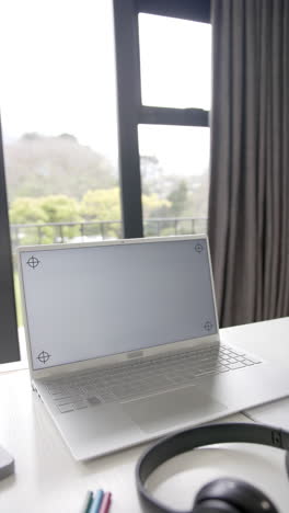 vertical video of laptop with copy space on screen and headphones on desk, slow motion