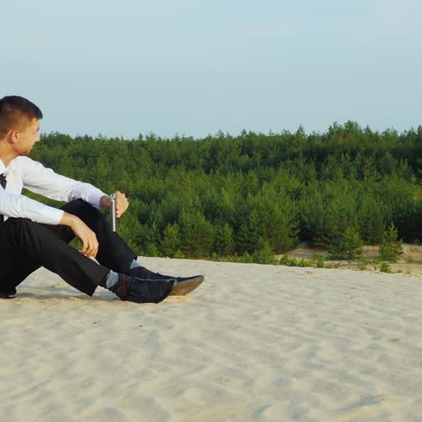 a businessman drinks alcohol and sits on the sand