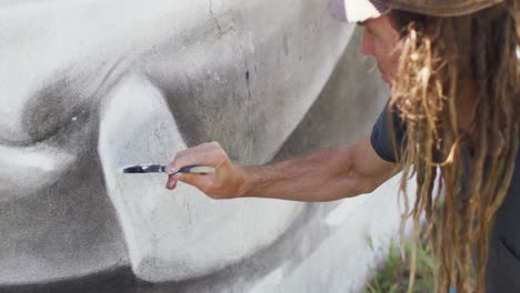 video of caucasian male artist with dreadlocks painting whale mural on wall