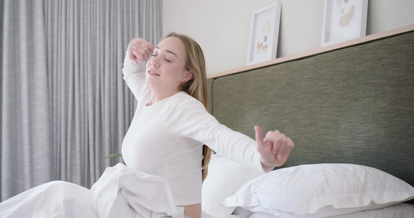Female waking in bed from daylight, reaching for pink smartphone to check screen, stretching