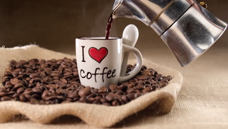 pouring coffee on i love coffee cup from moka machine on jute background and coffee beans