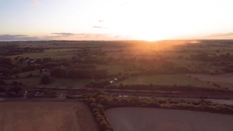 Slowly-flying-towards-the-sunset,-as-a-train-passes-through-the-bottom-of-the-shot