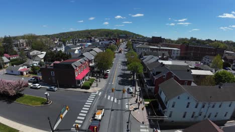 FPV-Flug-über-Die-Hauptstraße-Einer-Amerikanischen-Stadt-Mit-Bäumen-Und-Grünen-Hügeln-Im-Hintergrund