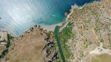 Aerial-top-down-view-of-cliffs-and-waves-breaking-in-the-sand-in-Crete,-Greece,-panning-out-to-sea
