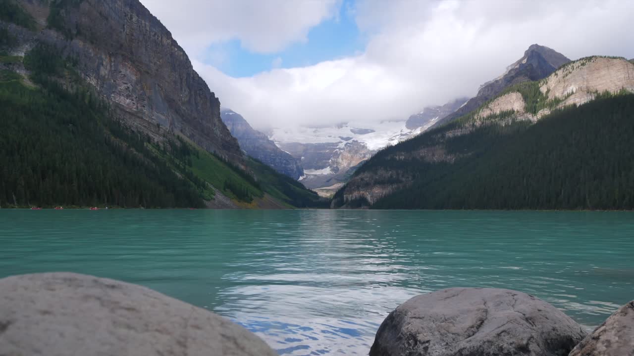 vista panorámica del lago louise, uno de los lagos más famosos del parque nacional de banff, alberta, canadá, en verano durante el día después de llover con nubes en el cielo y gente en canoa en el lago